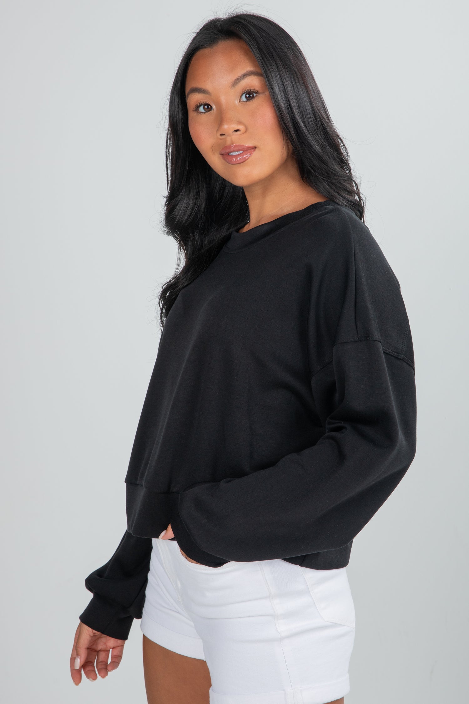 Woman wearing a black oversized sweatshirt and white shorts on a plain background