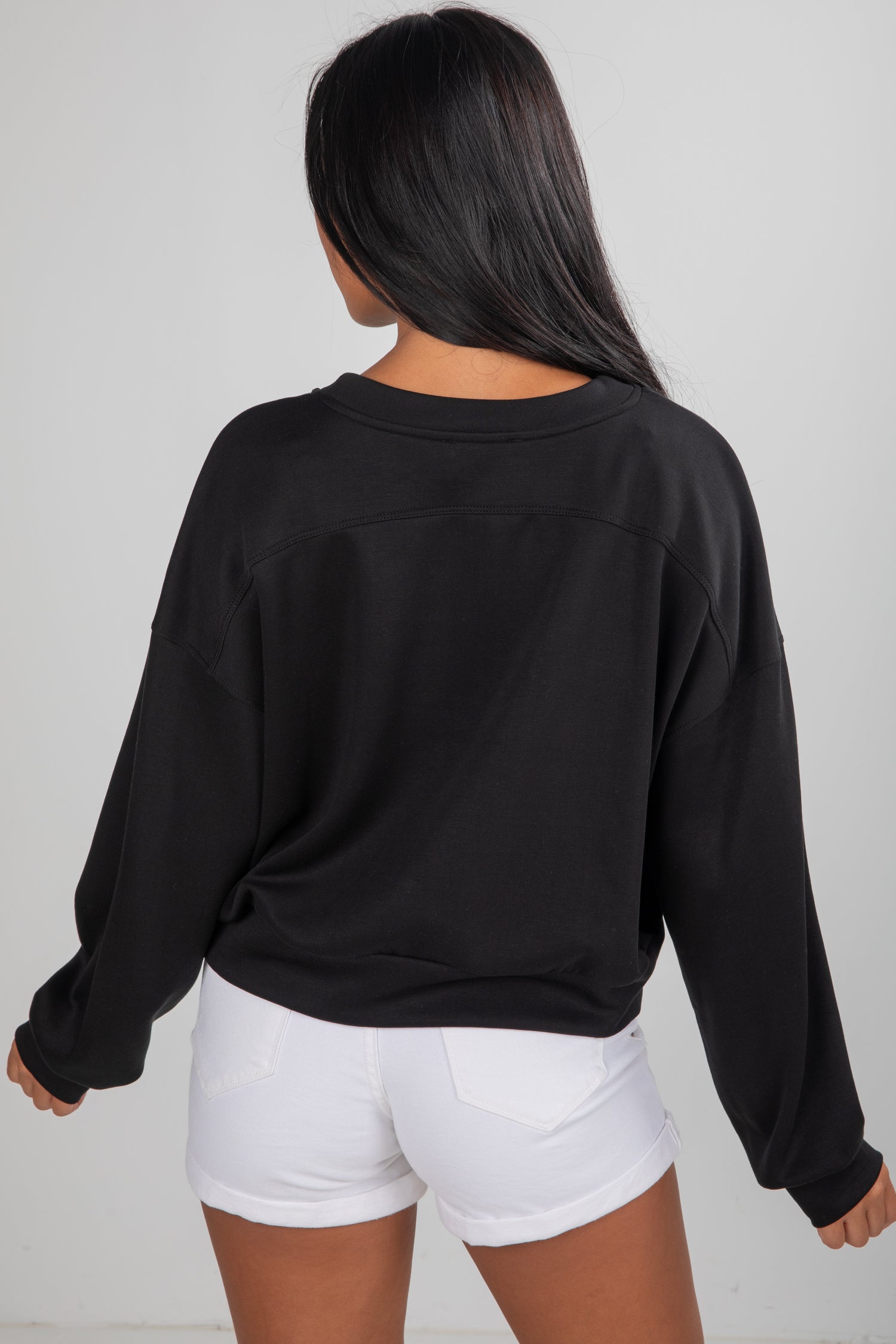 Person wearing a black oversized sweatshirt and white shorts on a plain background