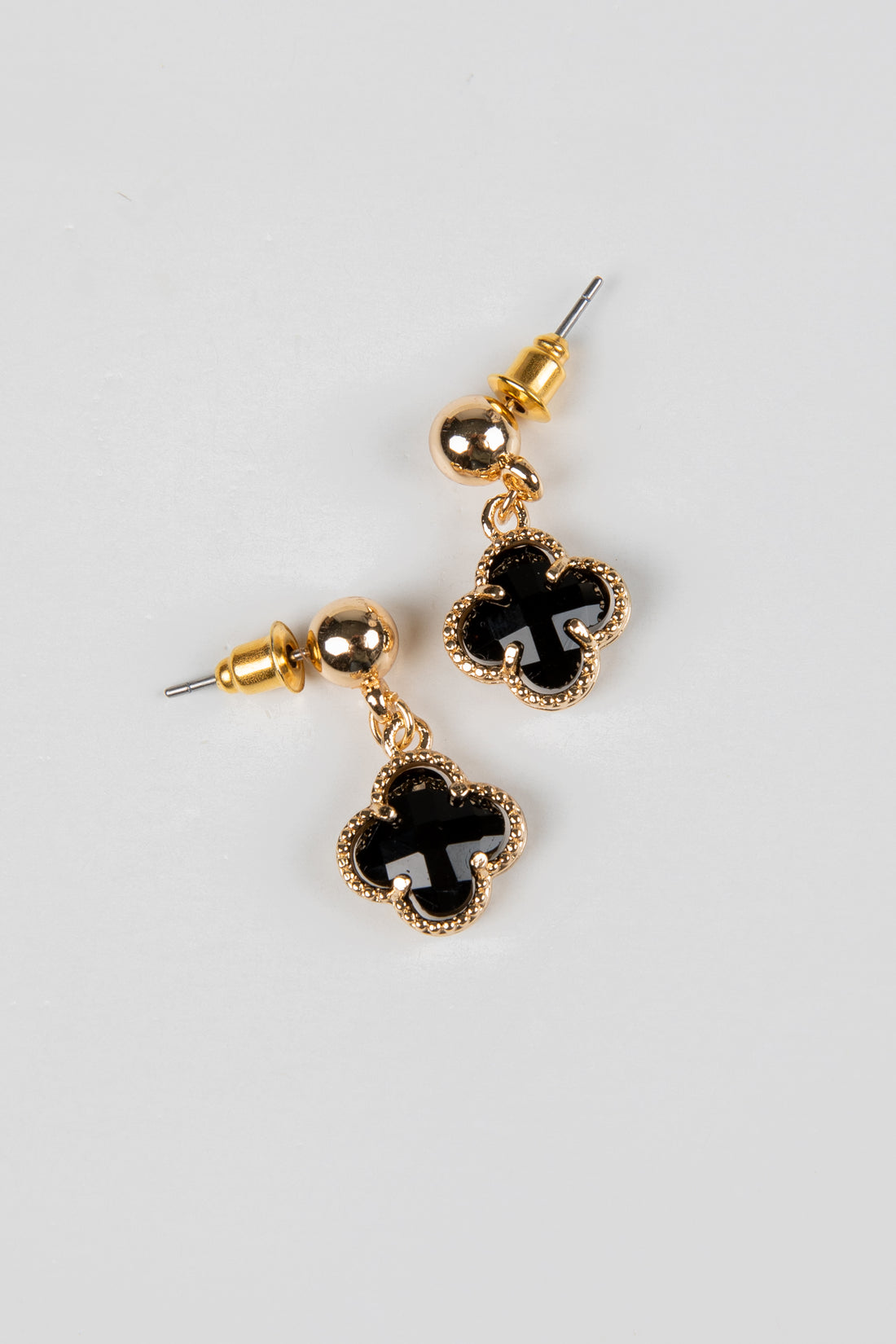 Gold earrings with black clover-shaped stones on a light gray background