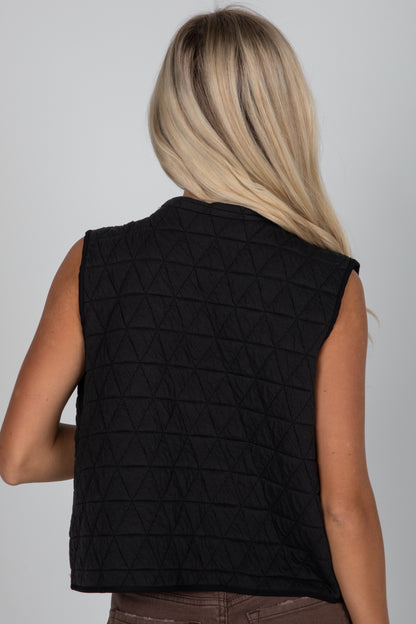 Person wearing a black quilted vest on a plain background