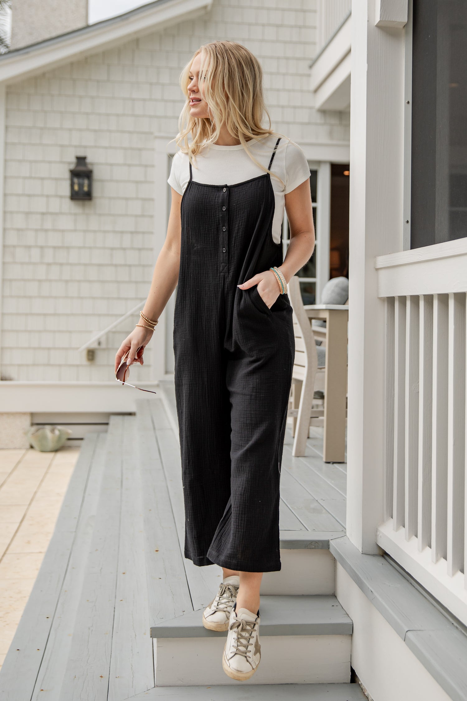 Woman in black overalls and white shirt standing on a porch