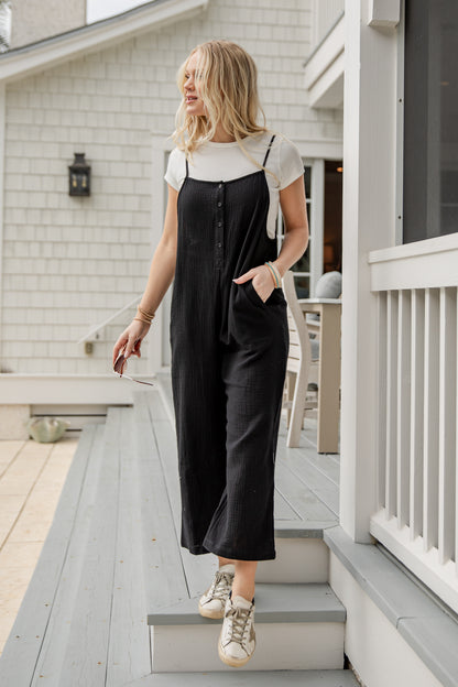 Woman in black overalls and white shirt standing on a porch