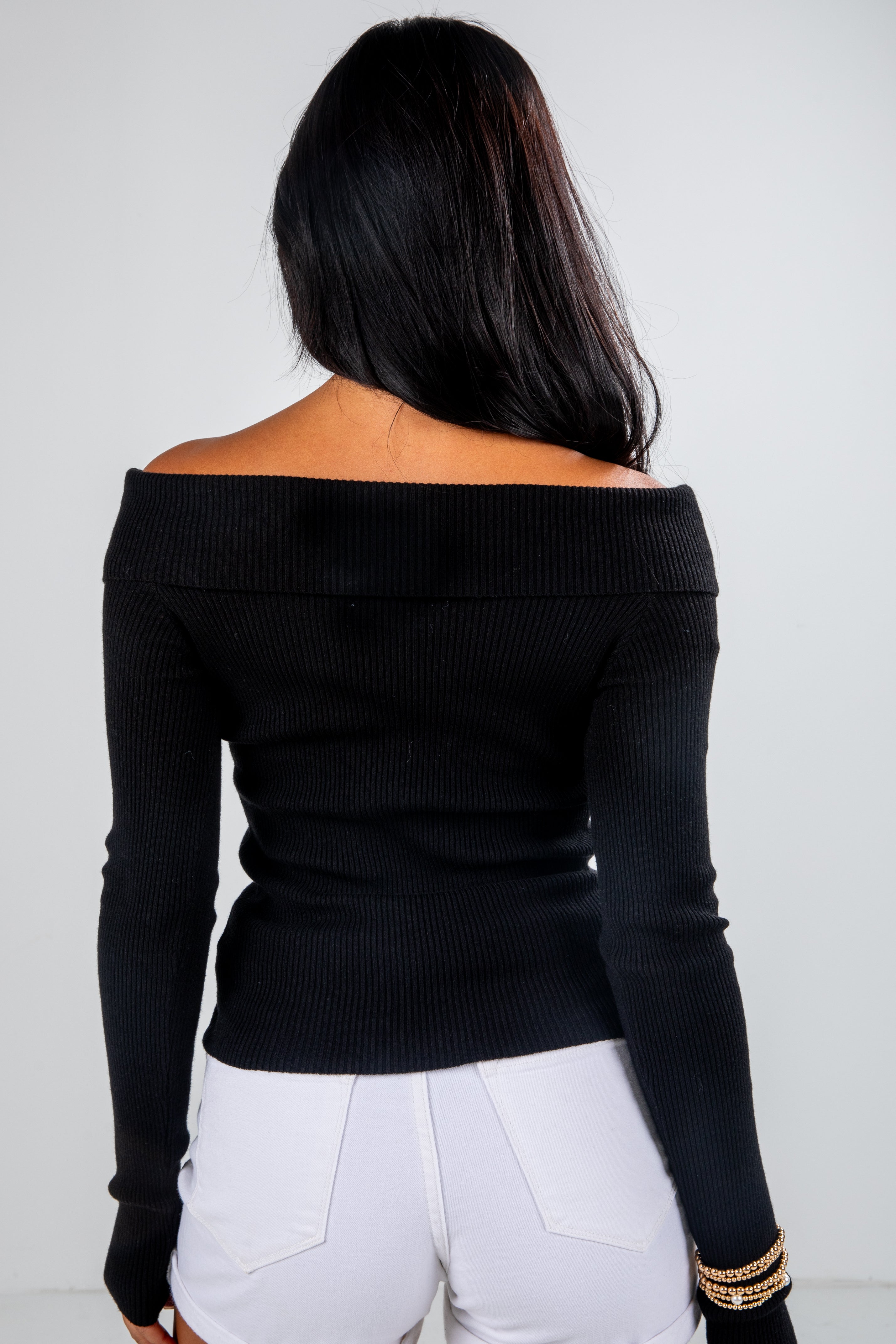 Person wearing a black off-shoulder top and white pants against a plain background