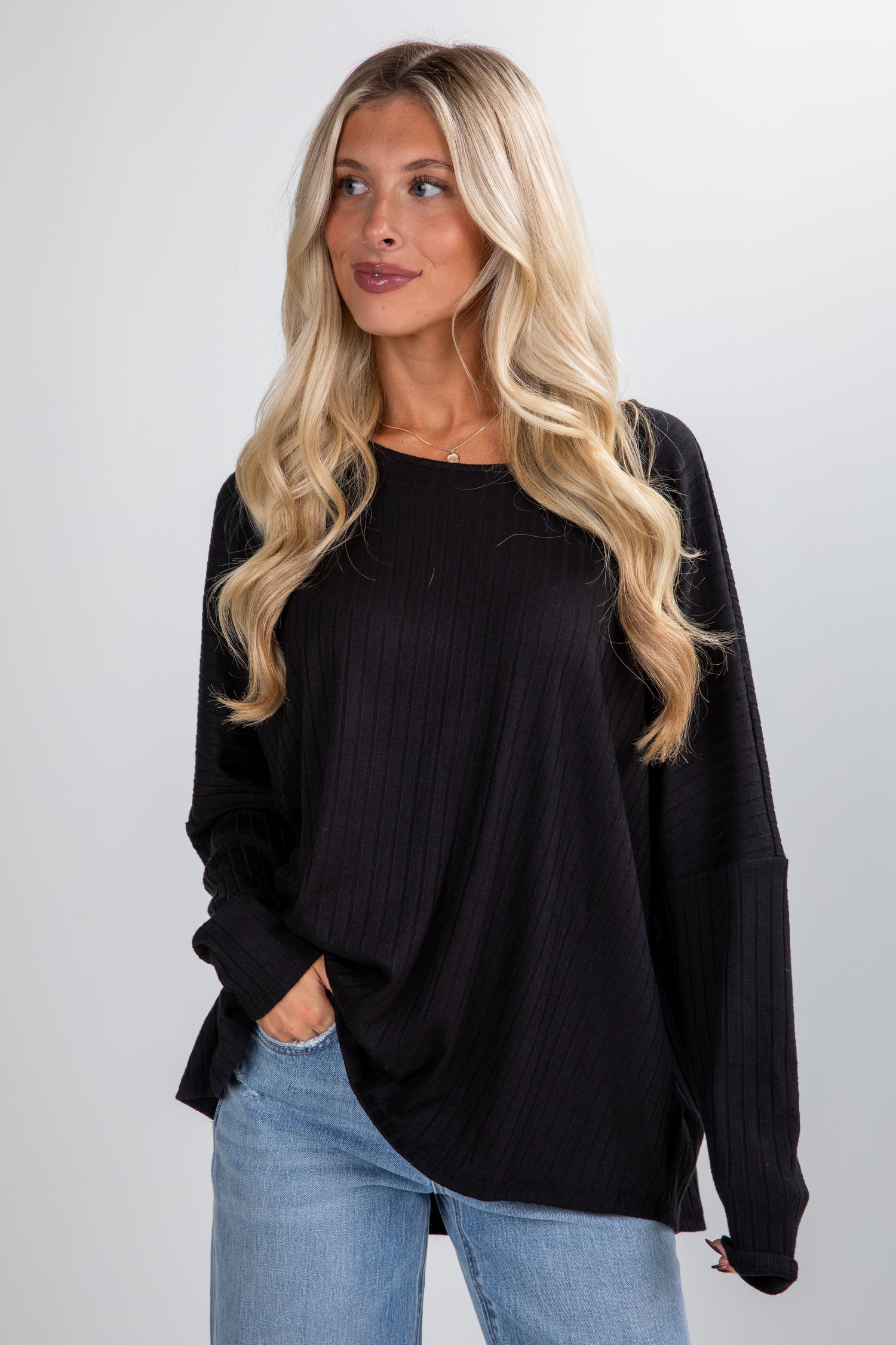 Woman wearing a black oversized sweater and light blue jeans against a plain background