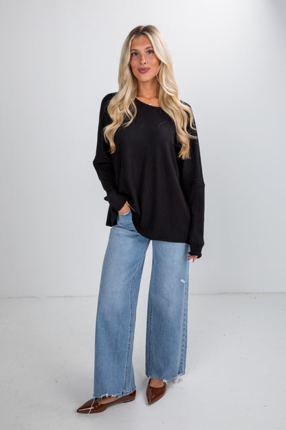 Woman wearing a black long-sleeve top and blue jeans on a white background