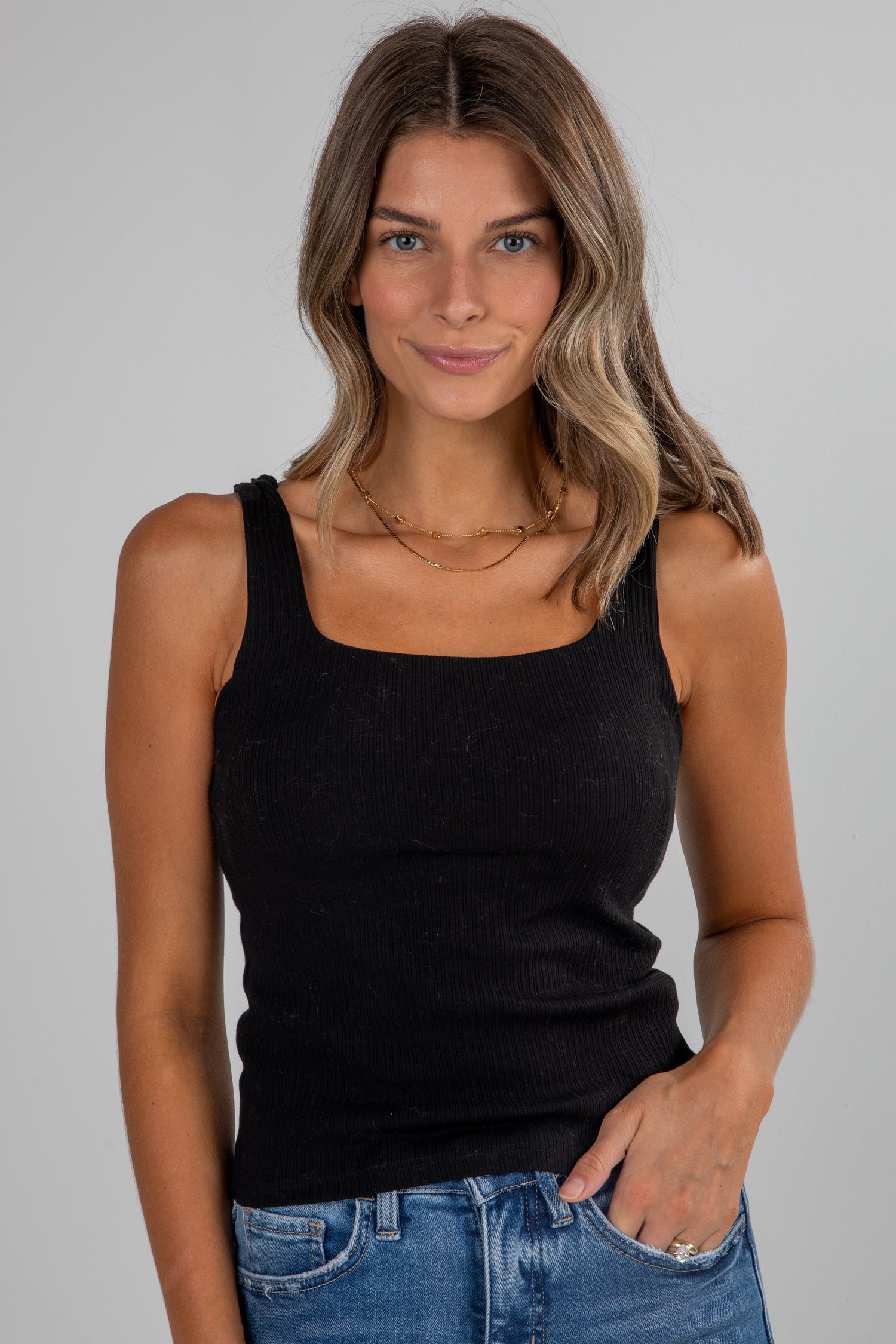 Woman wearing a black tank top and blue jeans against a gray background