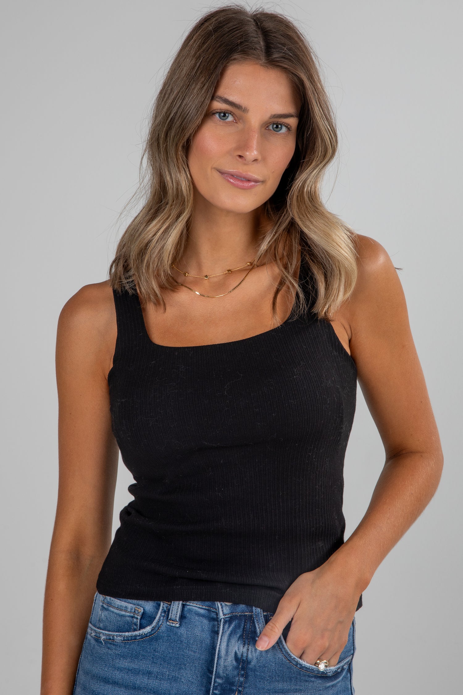 Woman wearing a black tank top and blue jeans against a gray background