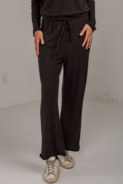 A person wearing dark brown wide-leg drawstring pants with a matching long-sleeve top and distressed white sneakers, standing in a plain studio setting.