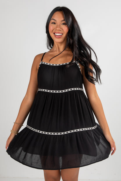 Woman wearing a black dress with white trim on a plain background