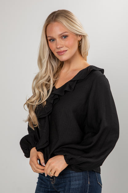 Woman wearing a black blouse with ruffled details on a plain background