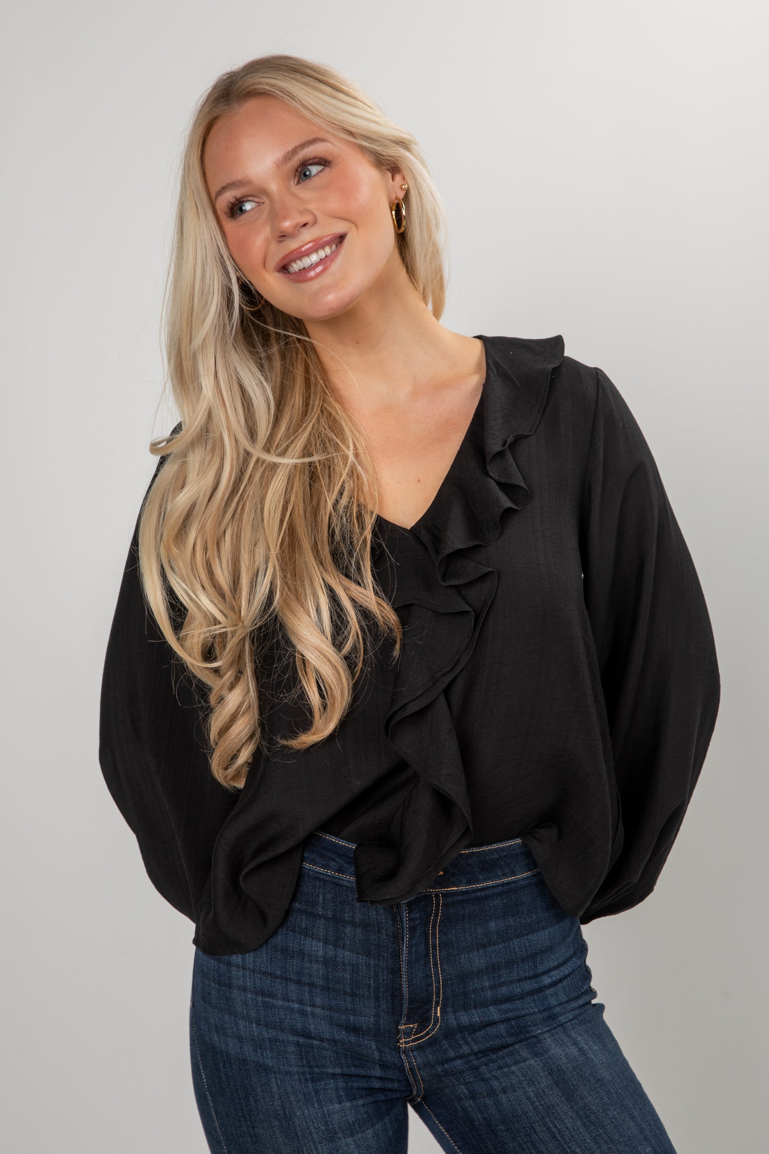 Woman wearing a black blouse with ruffles and blue jeans on a plain background