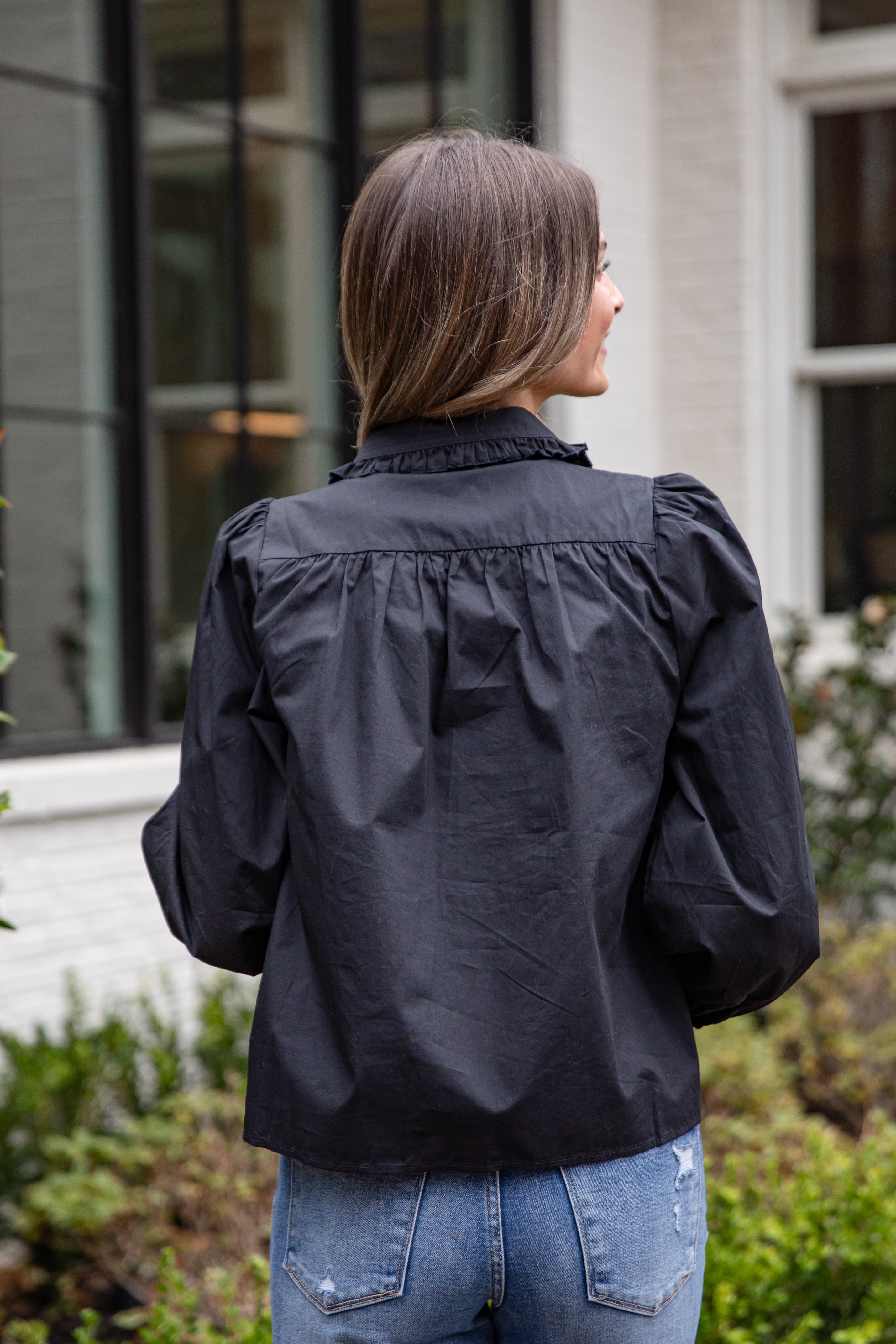 Person wearing a black jacket with ruffled shoulders outdoors