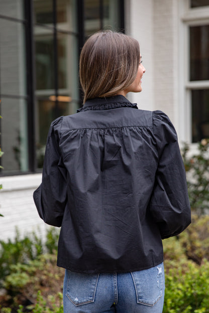 Person wearing a black jacket with ruffled shoulders outdoors