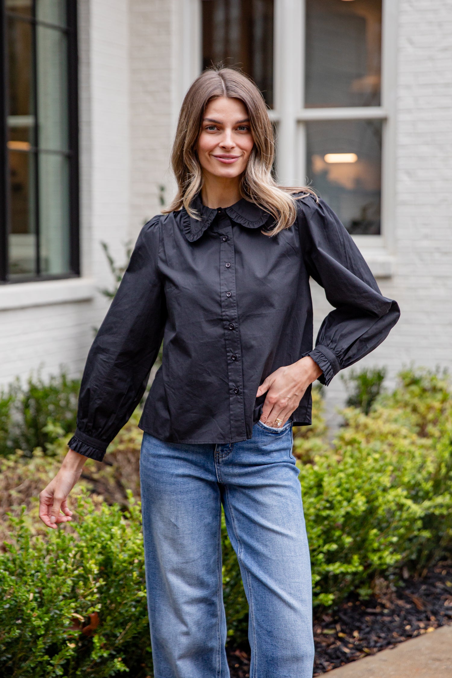 Woman wearing a black blouse and blue jeans standing outdoors.