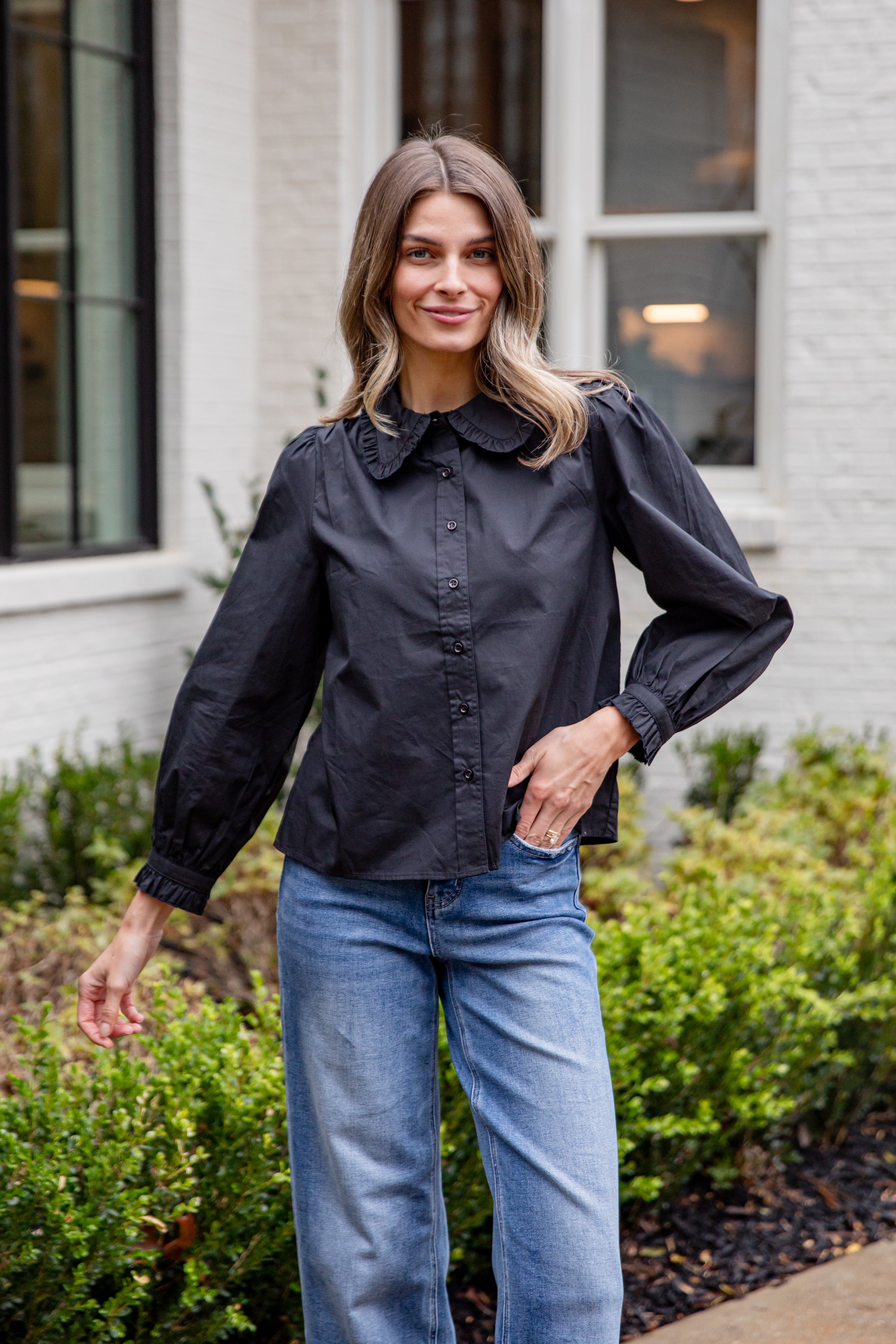 Woman wearing a black blouse and blue jeans standing outdoors.