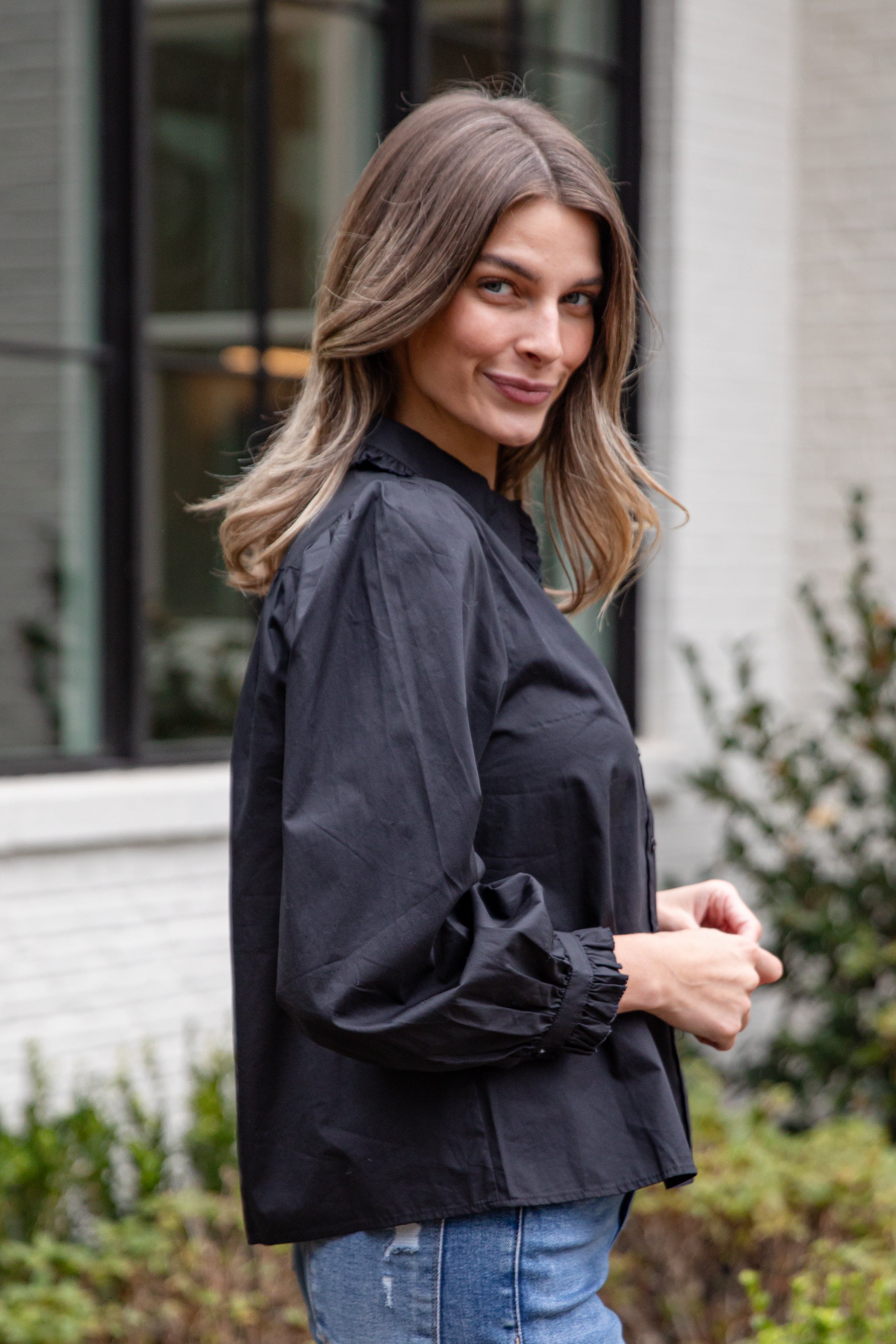 Woman wearing a black shirt and blue jeans standing outdoors.