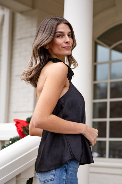Woman wearing a black sleeveless top and blue jeans standing on a porch.