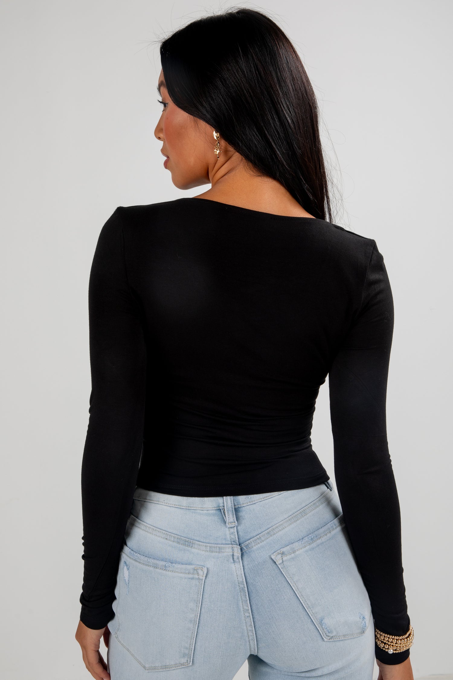 Person wearing a black long-sleeve top and light blue jeans against a plain background