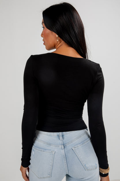 Person wearing a black long-sleeve top and light blue jeans against a plain background