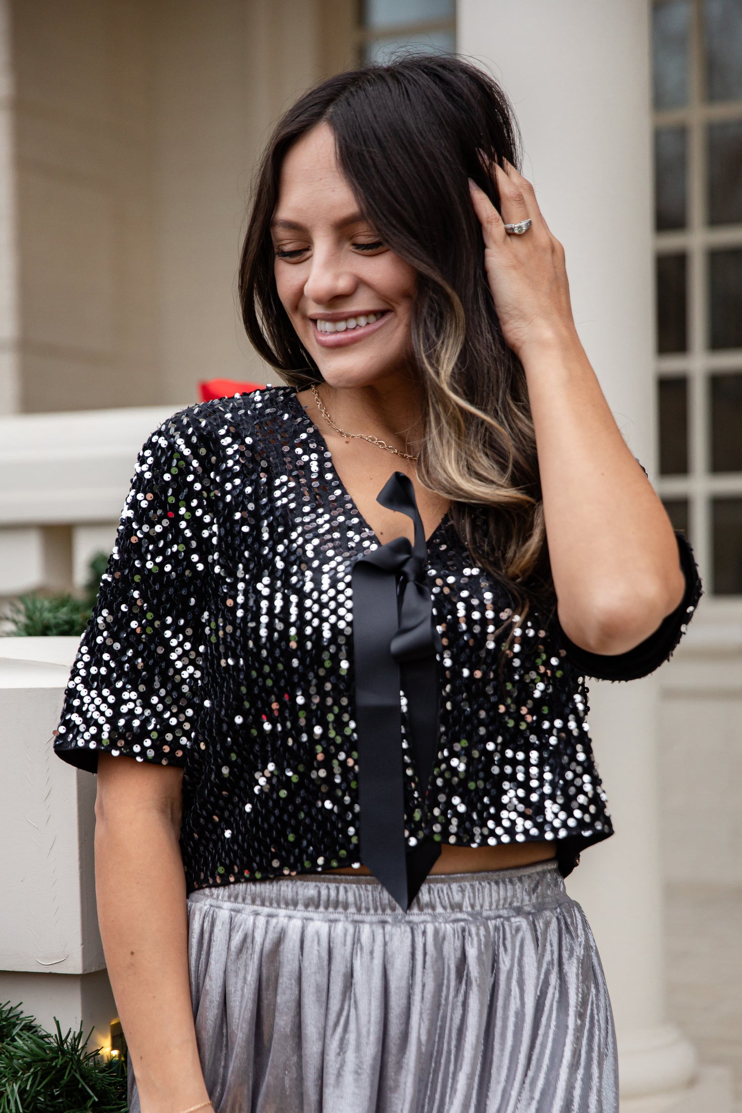 Woman wearing a black sequin top with a bow and silver pants outdoors.