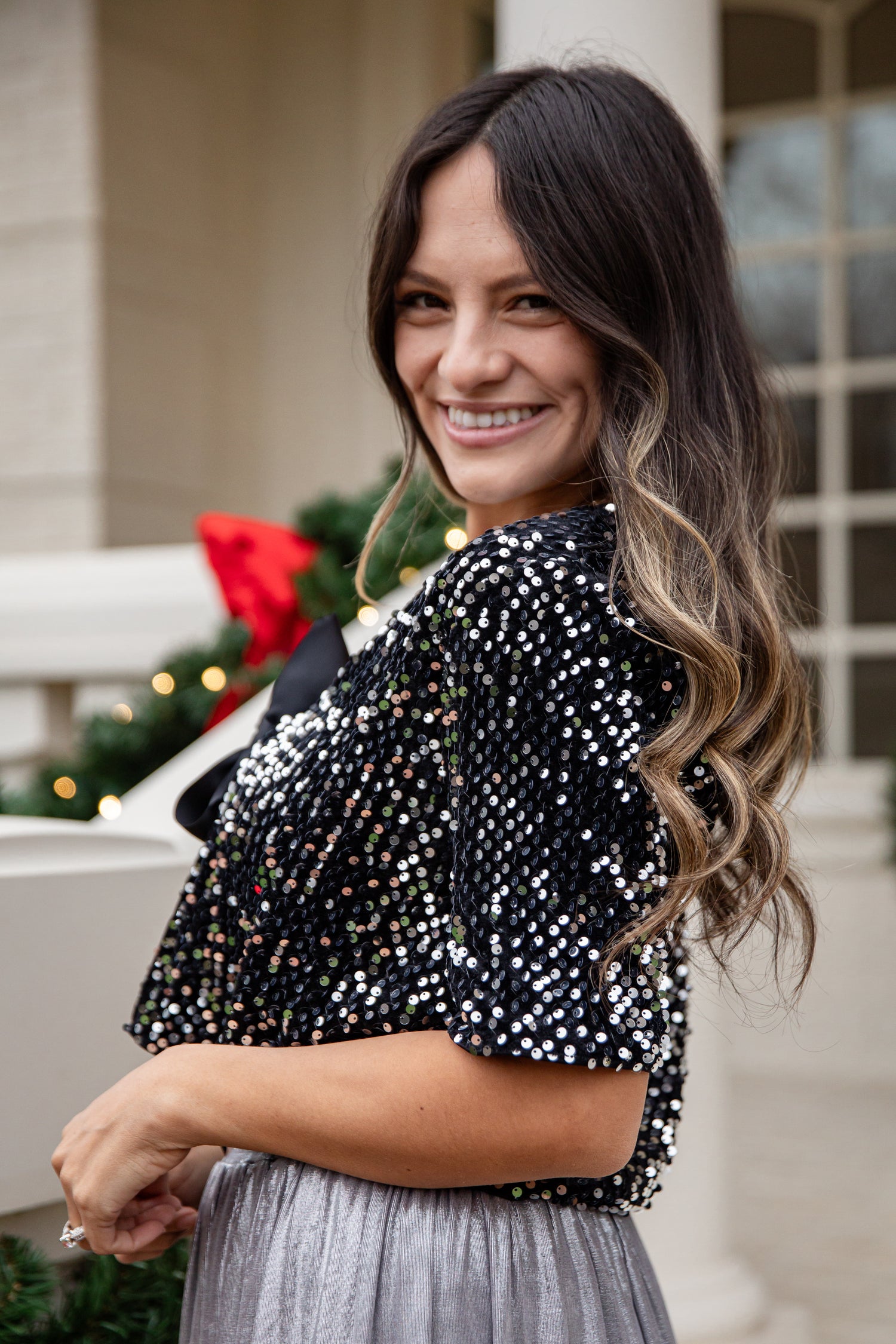 Woman wearing a black sequin top and gray skirt outdoors with Christmas decorations.