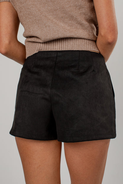 A close-up back view of a model wearing black high-waisted shorts and a beige ribbed knit top against a neutral gray background.