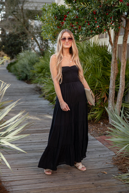 Woman in a black dress standing on a wooden path with greenery around