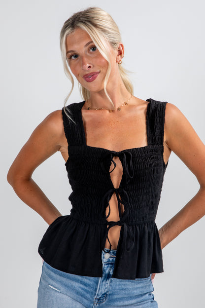 Woman wearing a black sleeveless top with lace-up details on a plain background