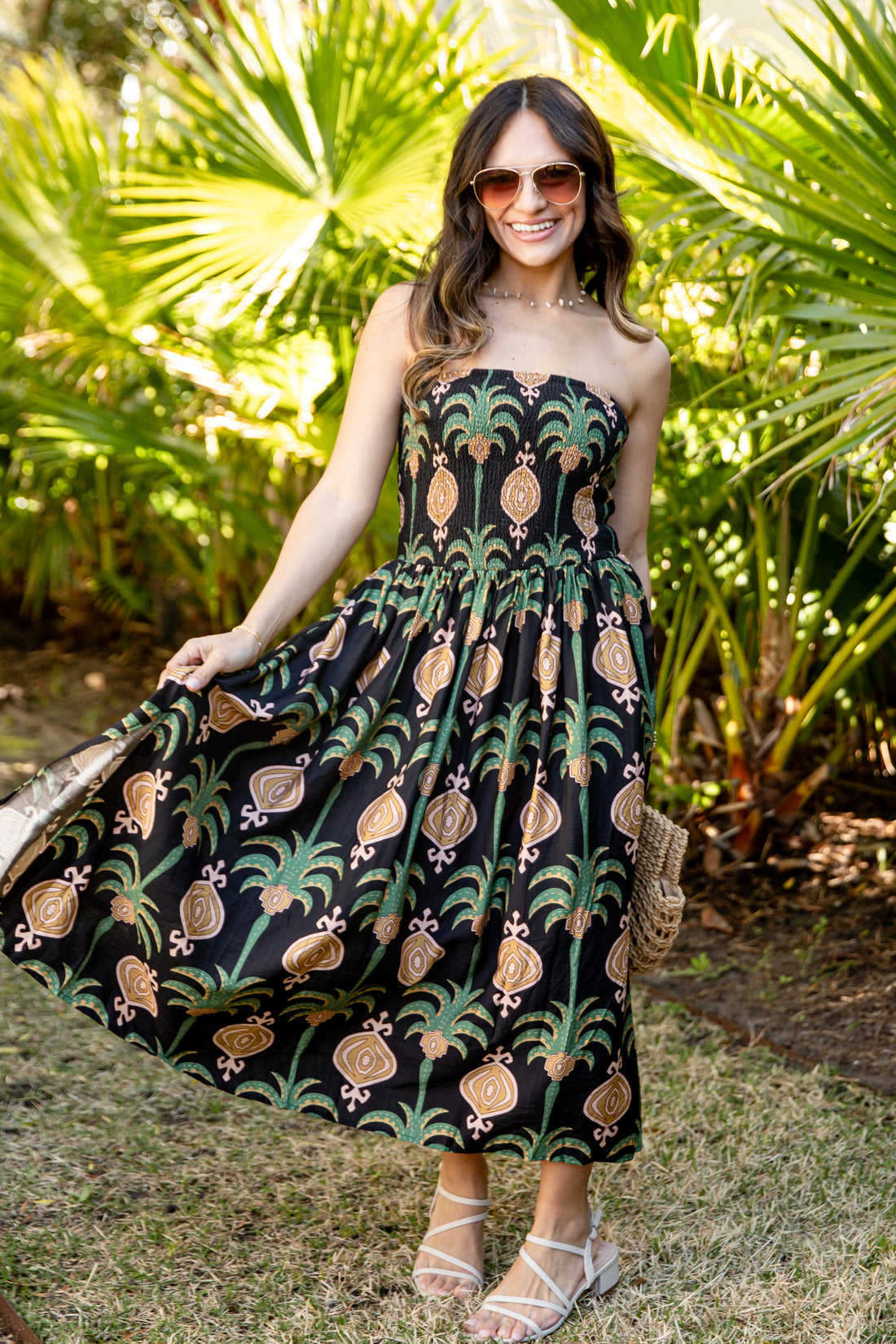 Woman in a strapless dress with pineapple pattern standing in a garden.