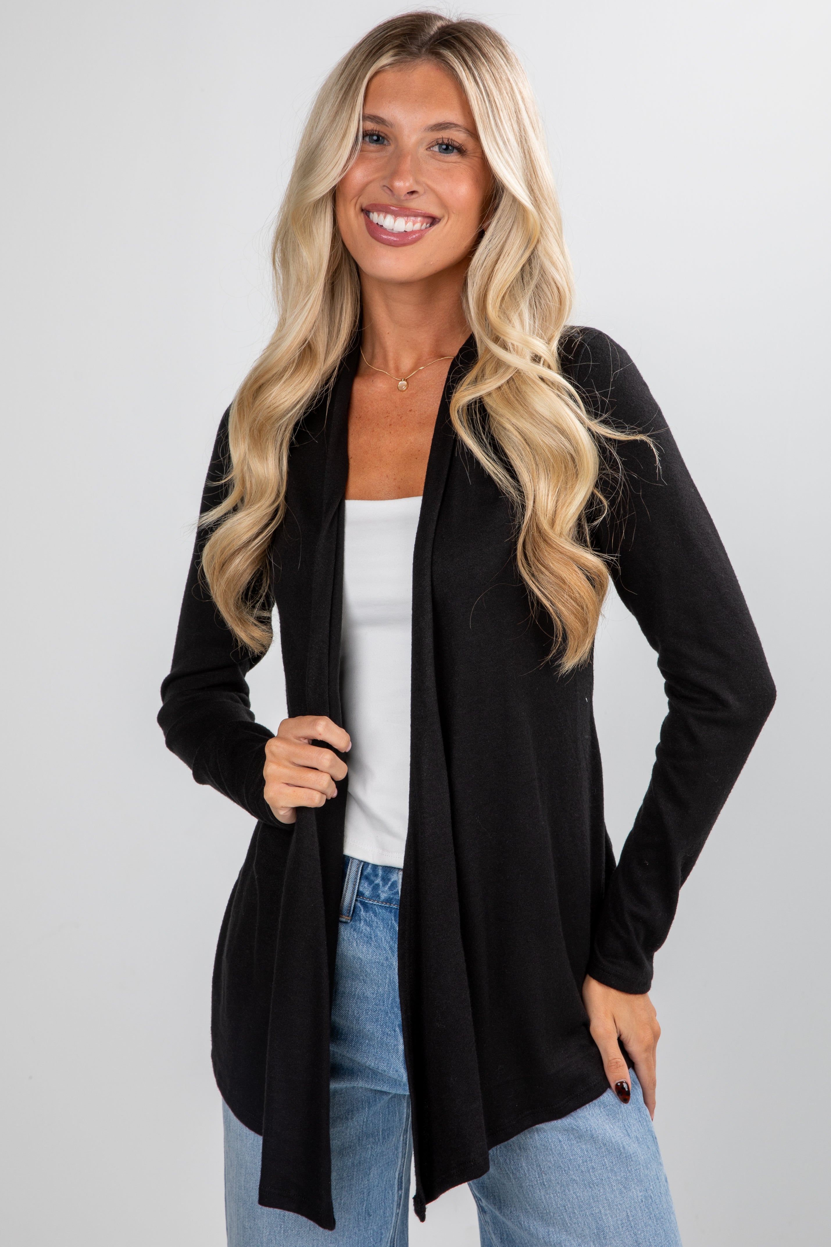 Woman wearing a black cardigan over a white top and blue jeans on a light gray background
