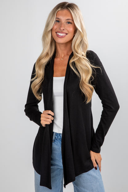 Woman wearing a black cardigan over a white top and blue jeans on a light gray background