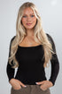 Woman with long blonde hair wearing a black top against a plain background
