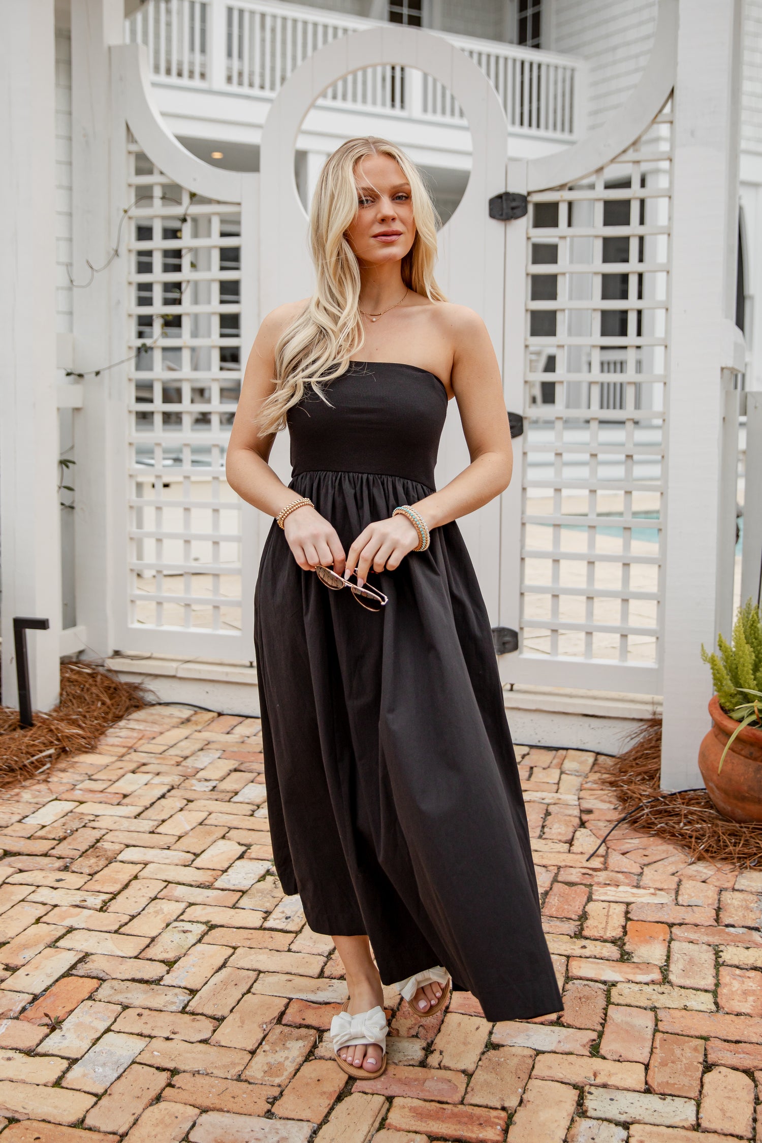 Woman in a black strapless dress standing on a brick patio.
