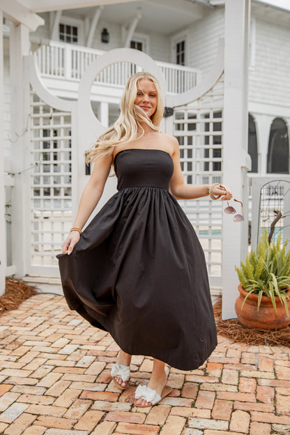 Woman in a black dress standing in front of a white house with a staircase.