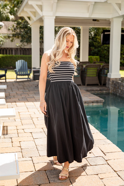 Woman in a black and white striped dress standing by a poolside.