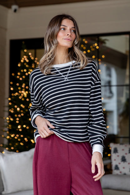 Woman wearing a striped sweater and pink pants in a cozy living room with Christmas decorations.