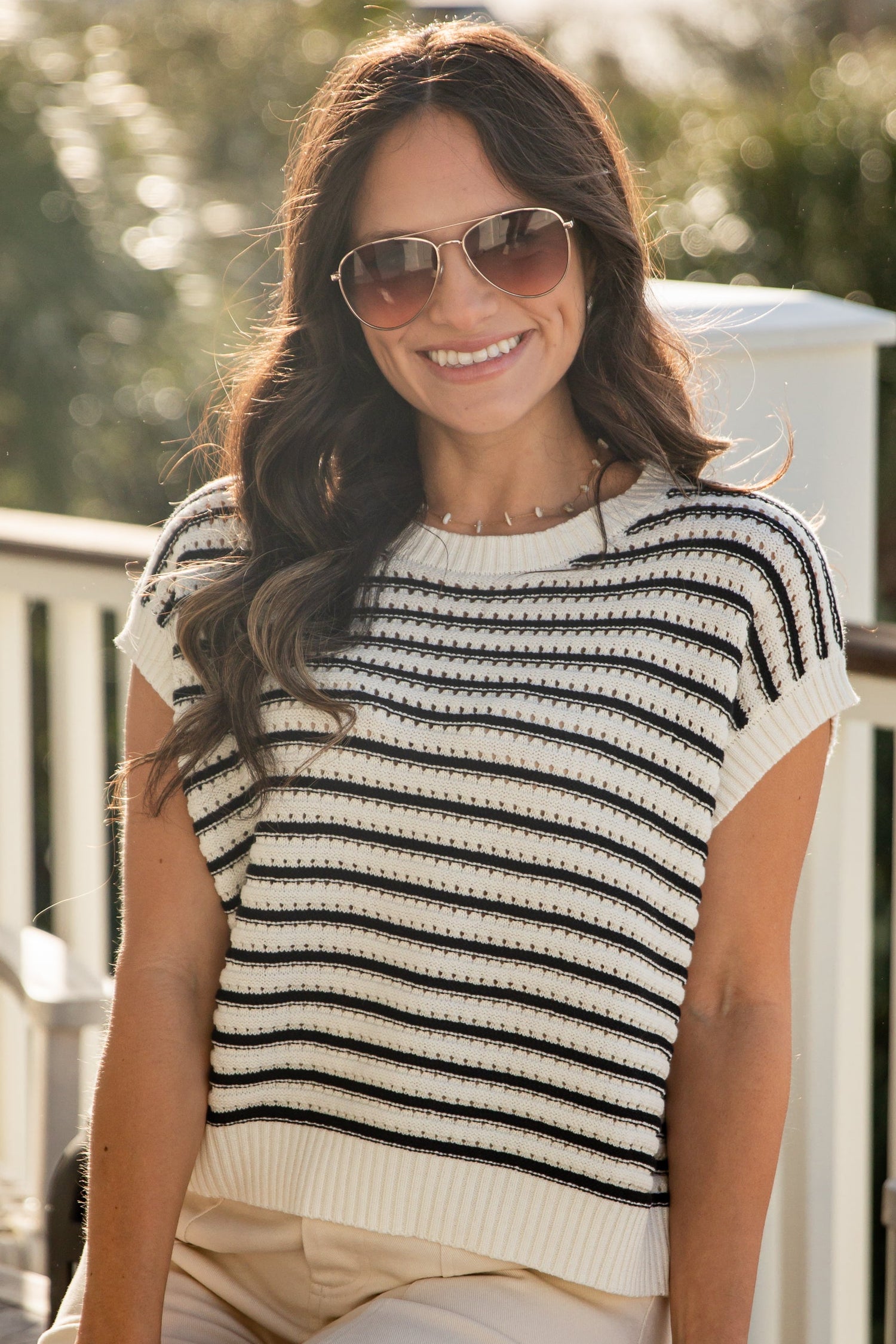Woman wearing a black and white striped top and beige pants on a sunny day.
