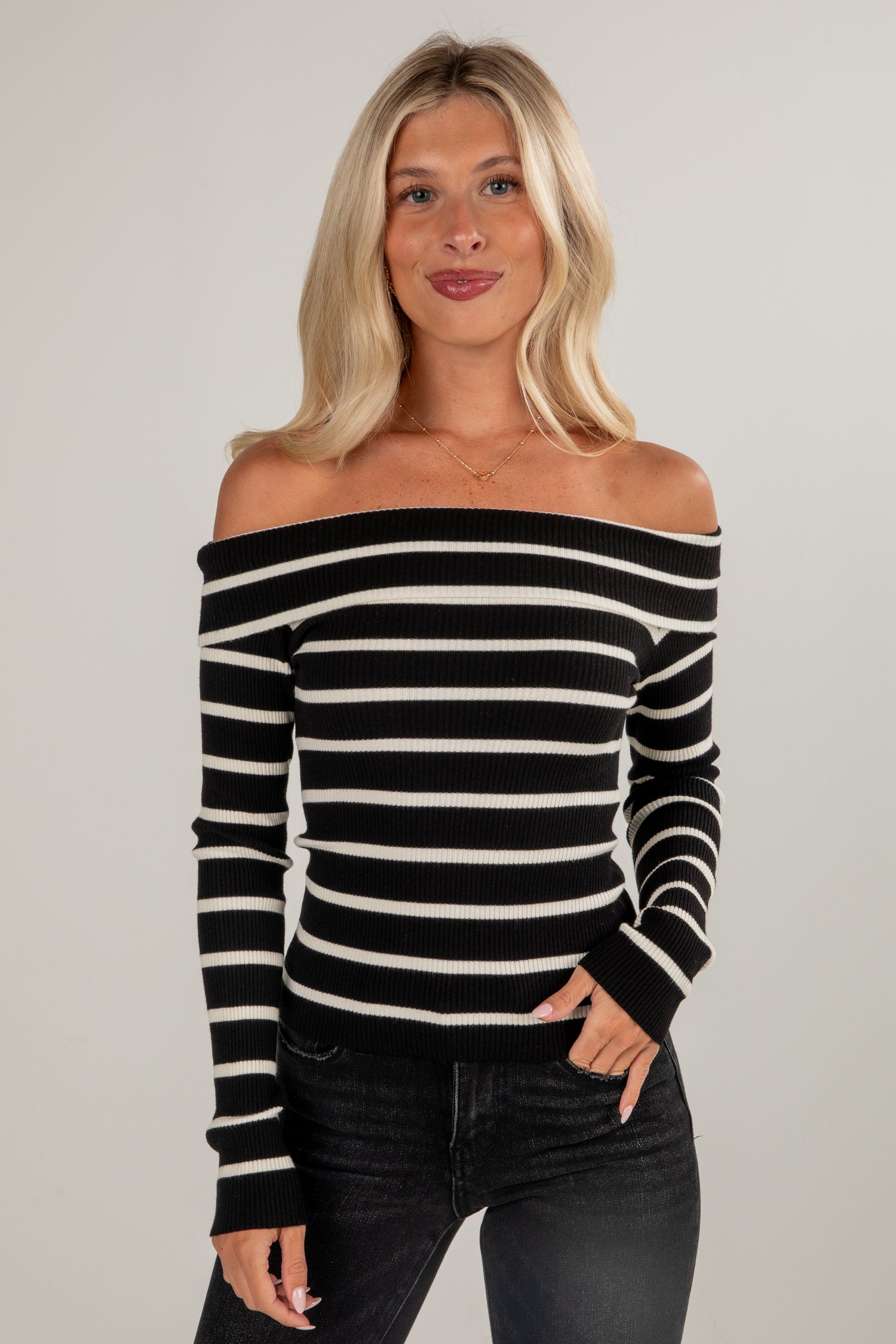 Woman wearing a black and white striped off-shoulder top against a gray background