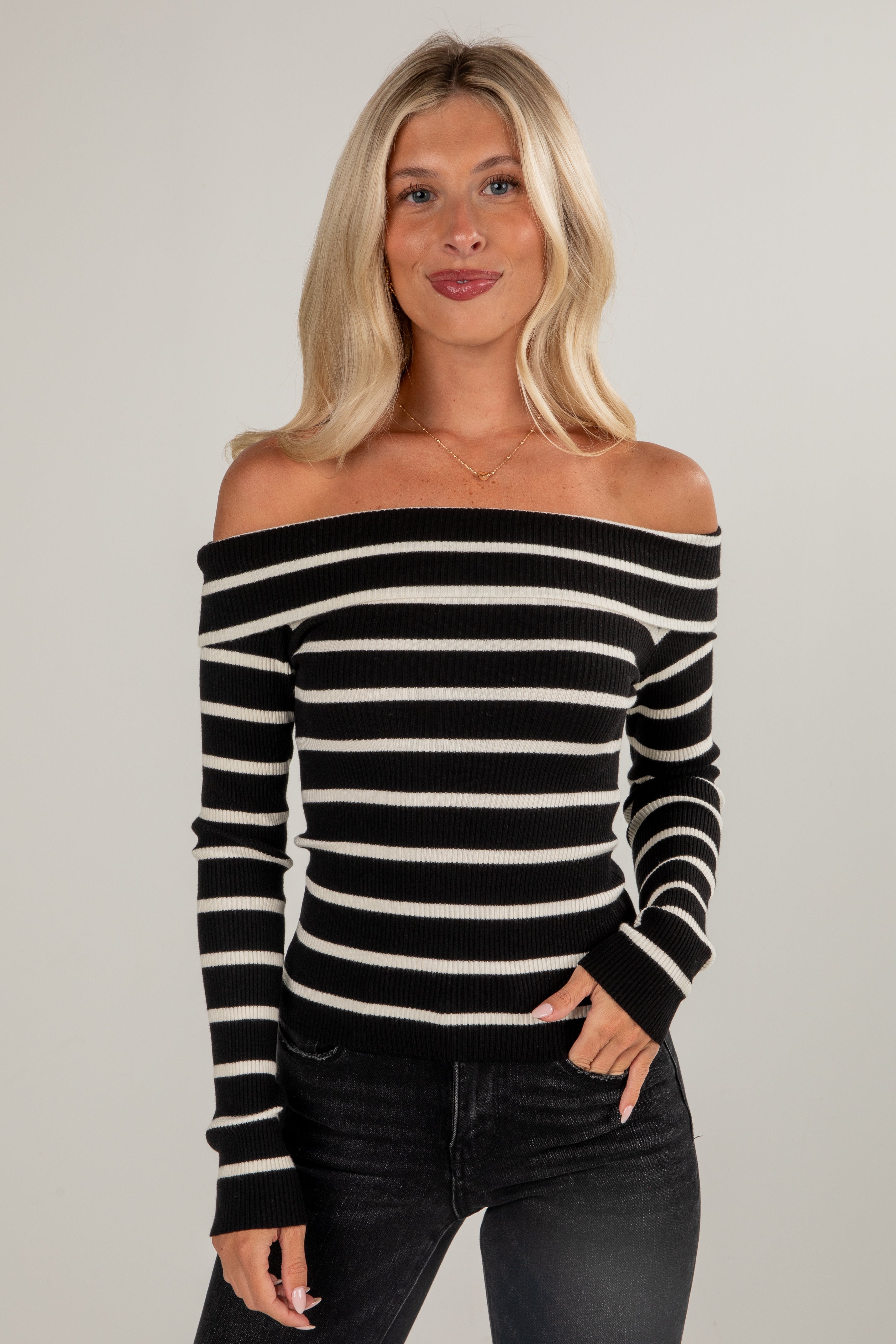 Woman wearing a black and white striped off-shoulder top against a gray background