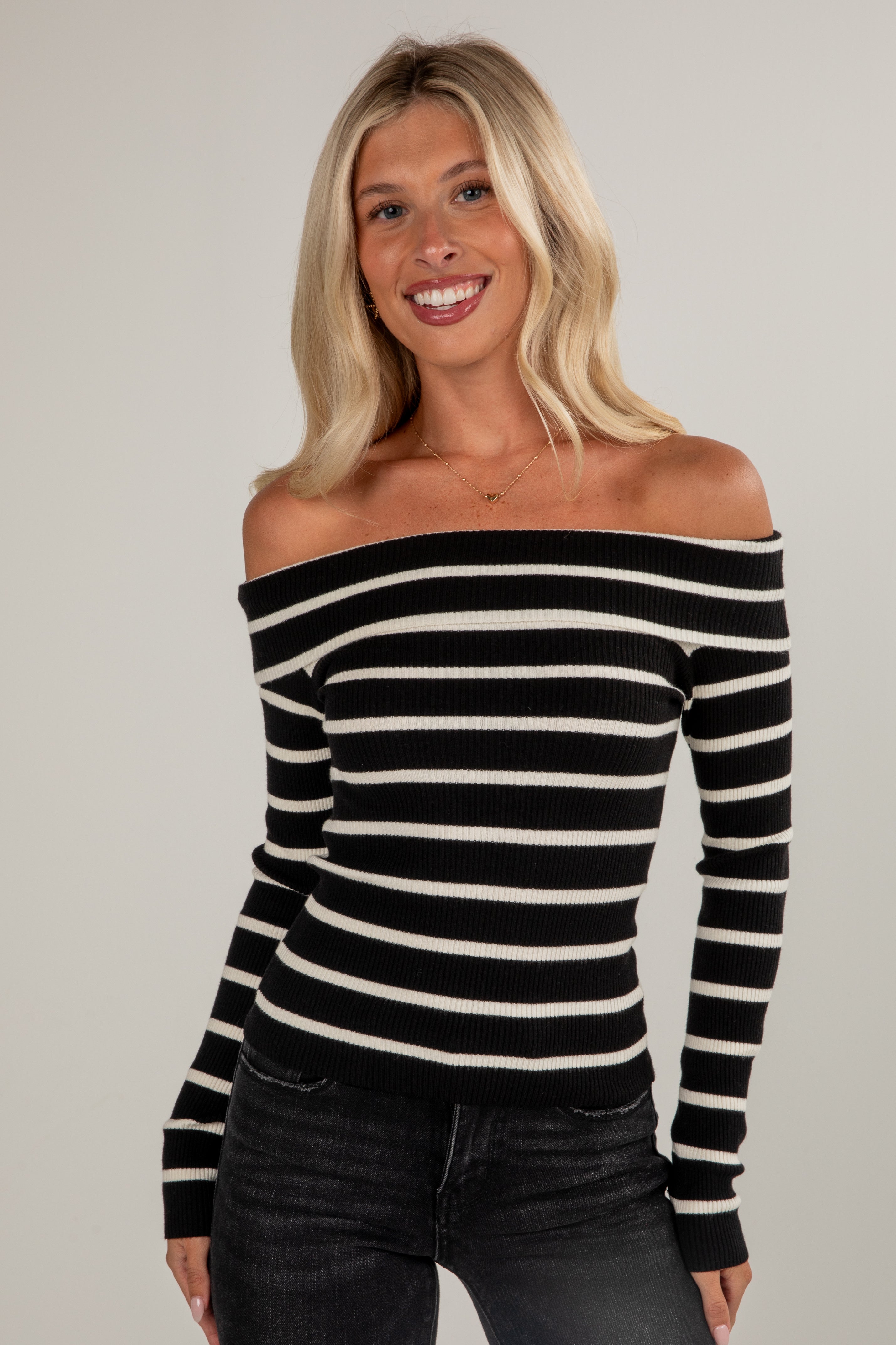 Woman wearing a black and white striped off-shoulder top against a plain background
