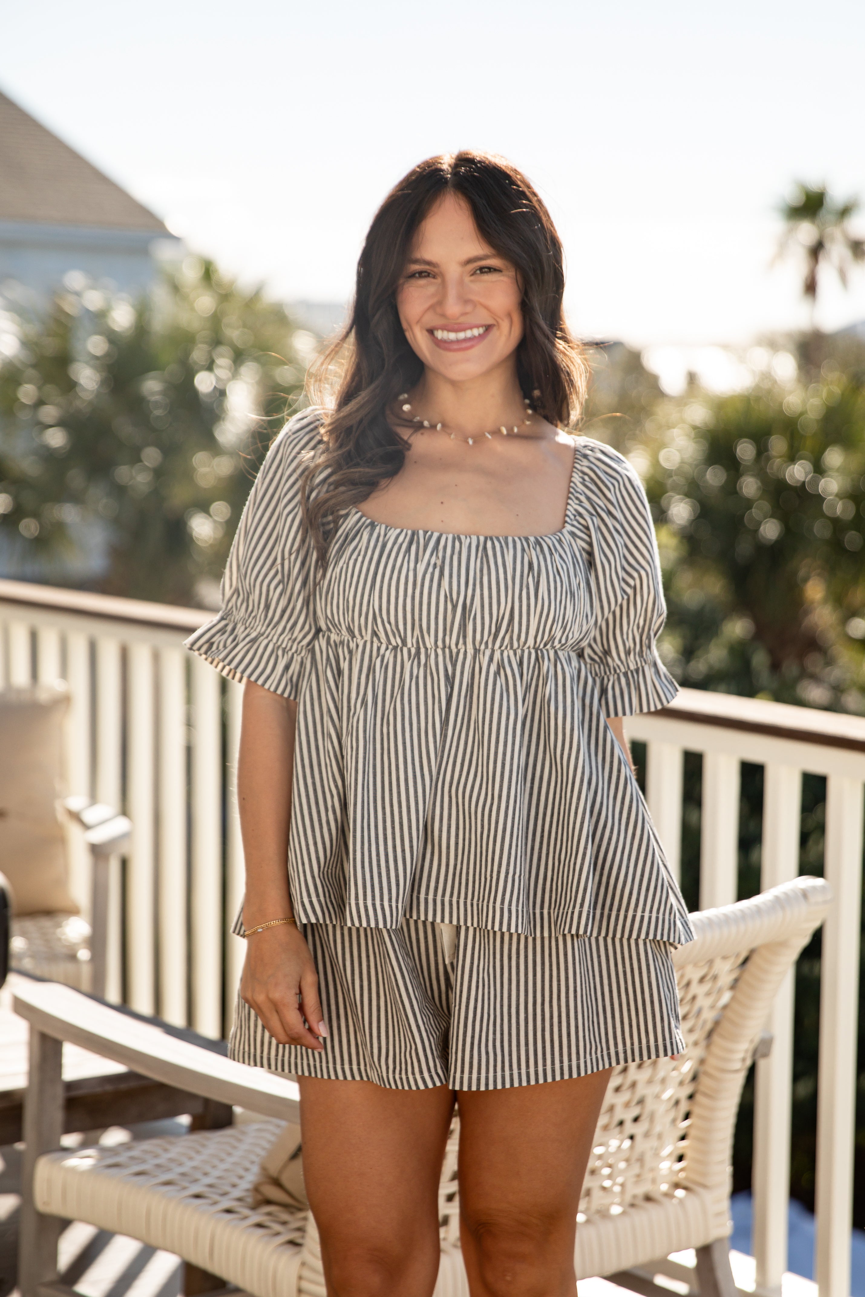 Woman in a striped dress sitting on a chair outdoors with trees in the background