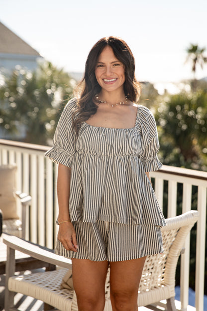 Woman in a striped dress sitting on a chair outdoors with trees in the background