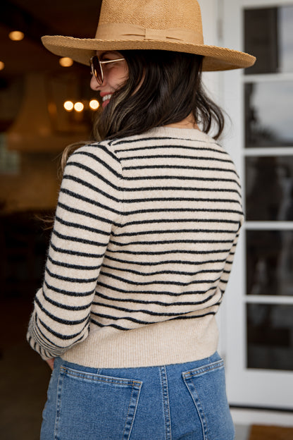Woman wearing a striped sweater, wide-brimmed hat, and sunglasses with a blurred indoor background