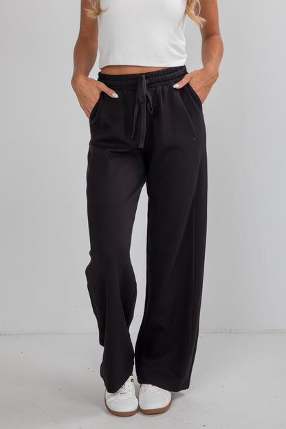 Person wearing black wide-leg pants with a white top on a plain background