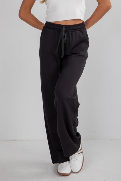 Person wearing black wide-leg pants and white top on a plain background