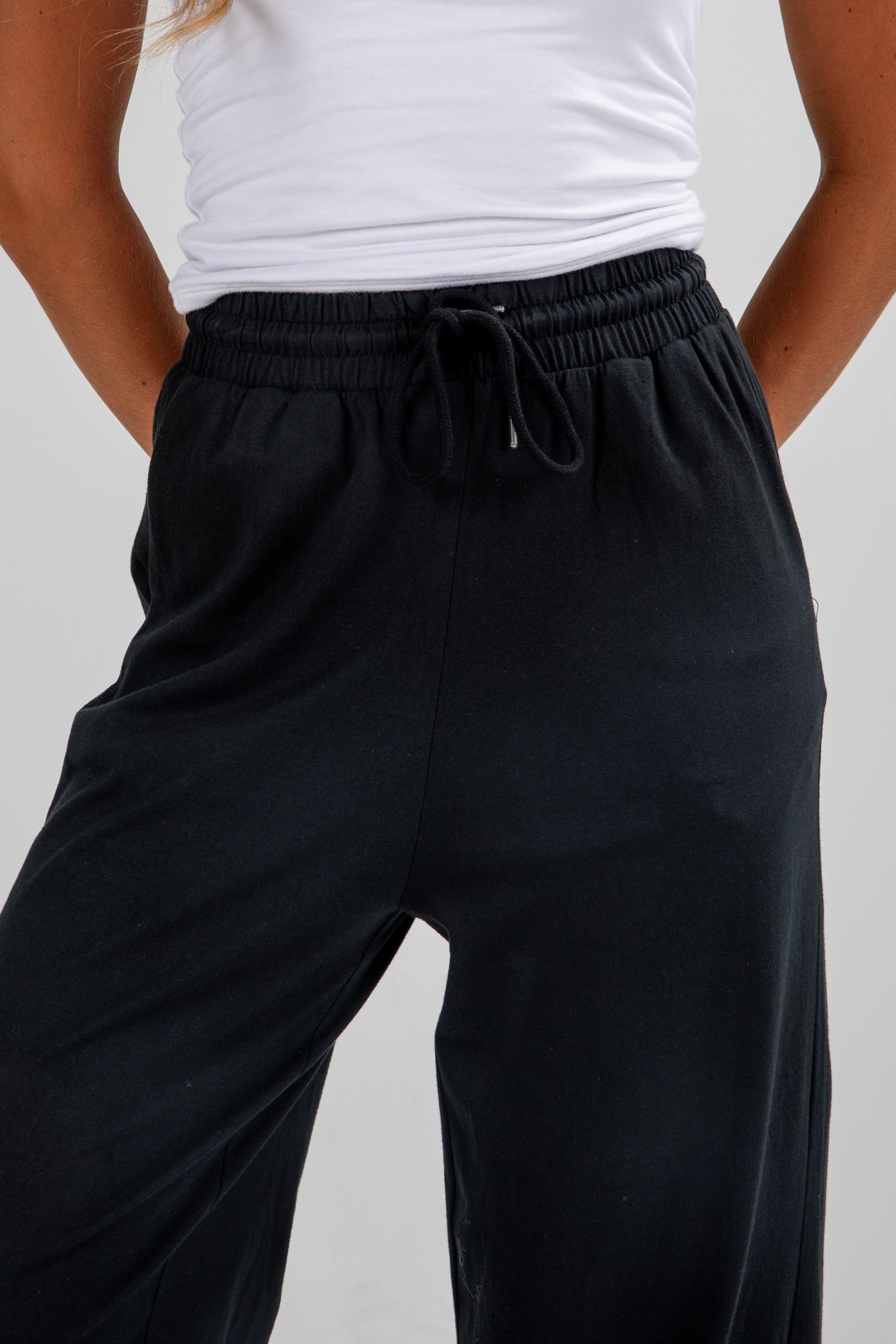 Person wearing black wide-leg pants and a white top on a plain background