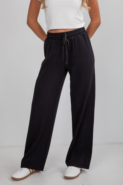 Person wearing black wide-leg pants with a white top on a plain background