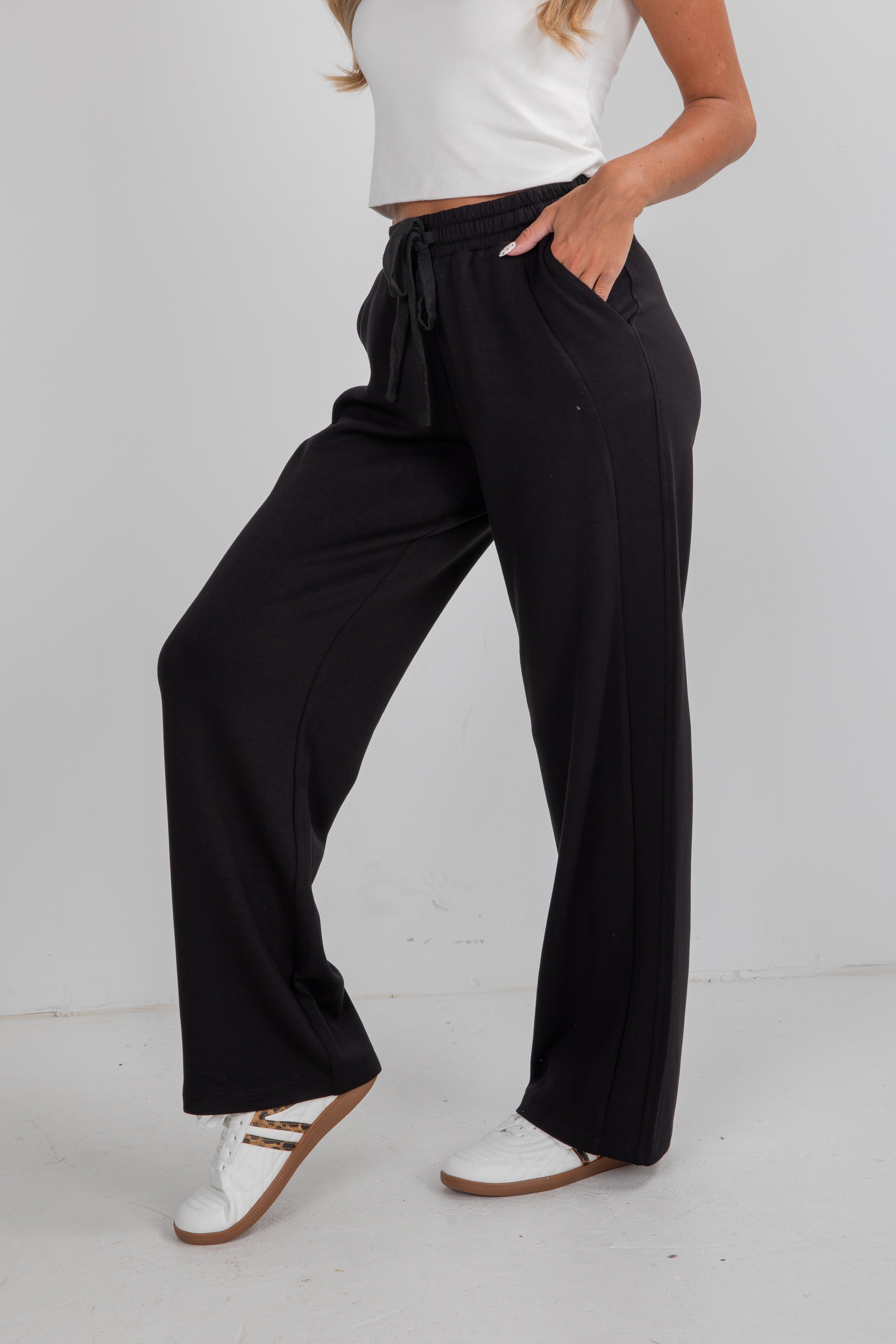Person wearing black wide-leg pants with a white top on a light gray background