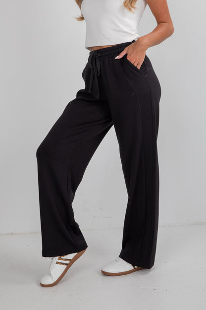 Person wearing black wide-leg pants with a white top on a light gray background