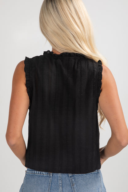 Person wearing a black sleeveless top with ruffled details on a plain background